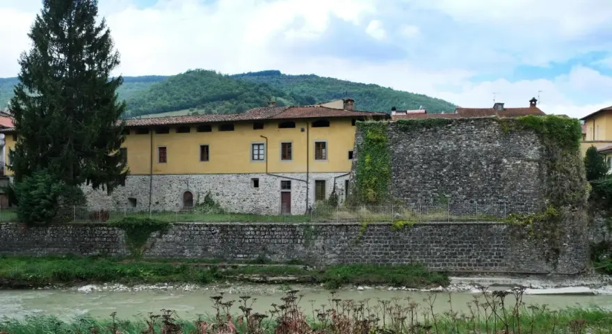 Pieve Santo Stefano: cosa vedere? Antica cinta muraria e palazzo storico affacciati sul fiume, tra colline verdi.