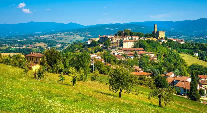 Borgo medievale in collina, un gioiello del Casentino cosa vedere. Case con tetti rossi, verde rigoglioso e un cielo azzurro intenso.