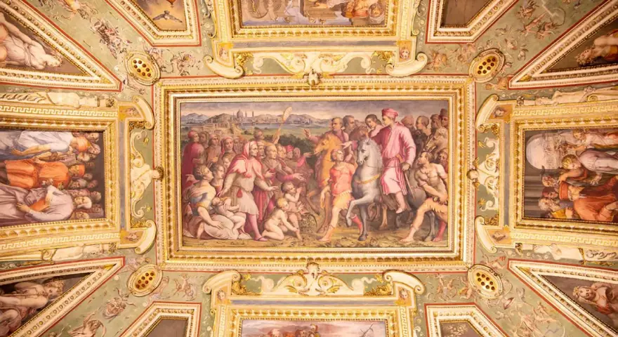 Soffitto affrescato con scene storiche e figure mitologiche, un capolavoro che evoca la grandezza del **Palazzo Vecchio**.