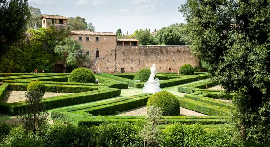 Giardini geometrici a San Quirico d'Orcia con statua bianca e edifici storici sullo sfondo.