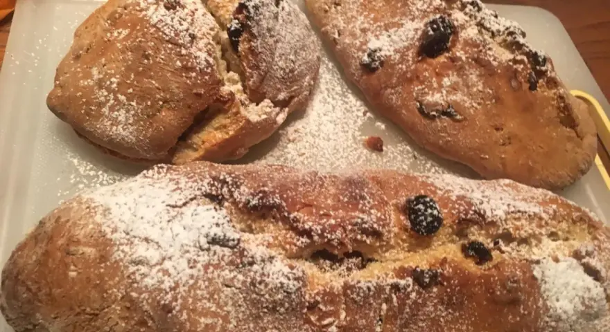Tre panini aretini dorati, cosparsi di zucchero a velo e uvetta, pronti per essere gustati.