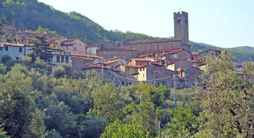 Antica villa basilica con torre campanaria, immersa nel verde di una collina toscana.