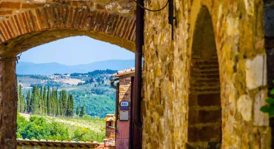 Arco in pietra che incornicia un panorama collinare toscano, con cipressi e vigneti, tipico dei borghi del Chianti.