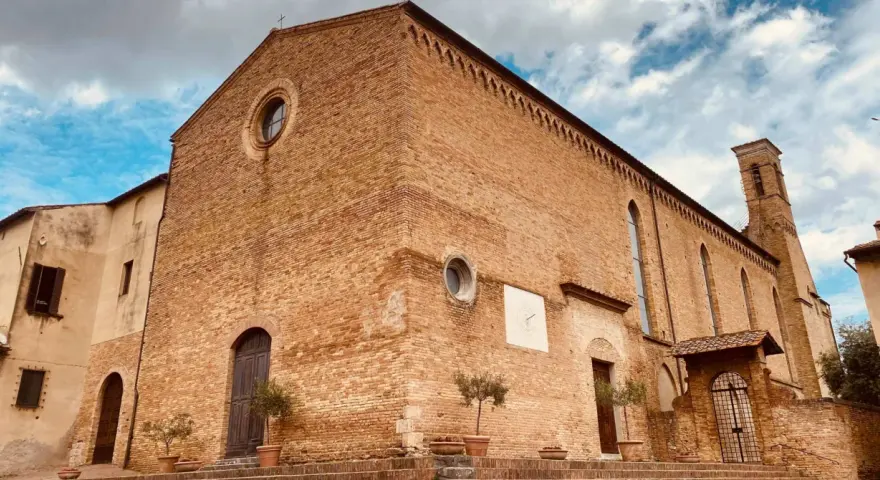 La **chiesa di Sant'Agostino** a San Gimignano, con la sua facciata in mattoni rossi e il campanile svettante, si staglia contro un cielo azzurro e nuvoloso.