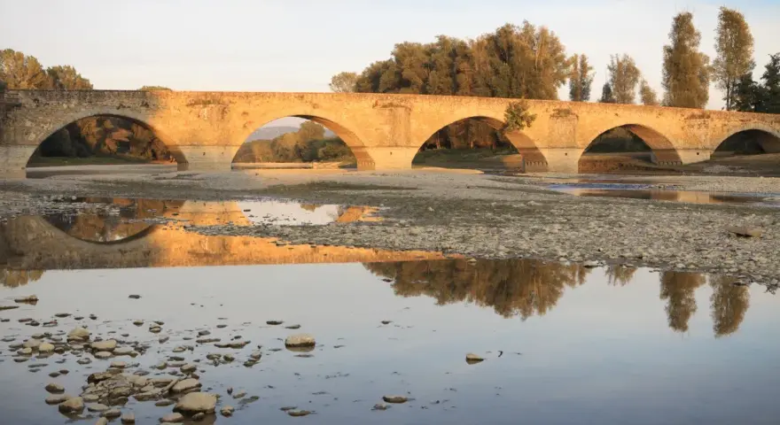 Ponte romanico con archi a tutto sesto, riflesso sull'acqua calma. I Setteponti di Arezzo, un'antica via, abbraccia la campagna toscana.