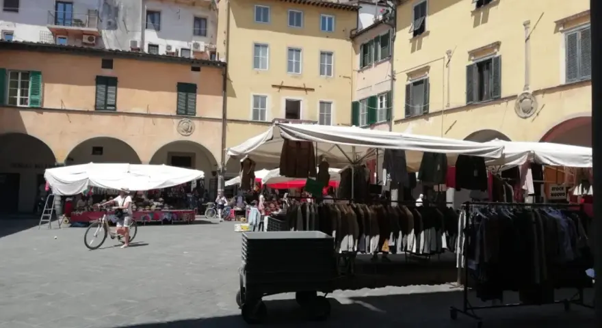 Mercato all'aperto nella piazza delle vettovaglie, con bancarelle di abbigliamento e persone che passeggiano.