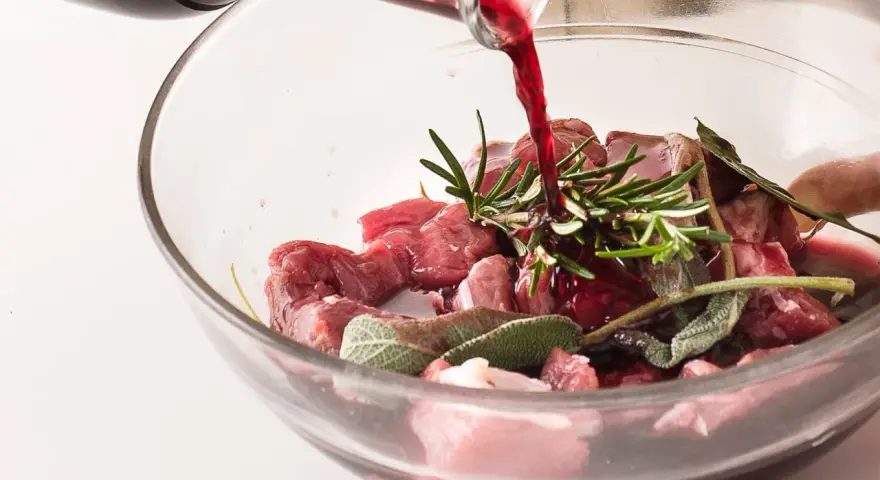 Vino rosso versato su cubetti di carne e aromi per macerare cinghiale.