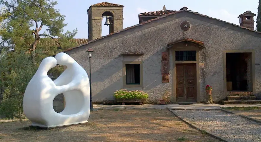 Scultura moderna di due figure abbracciate, simbolo di romena accoglienza, davanti a un edificio con campanile.