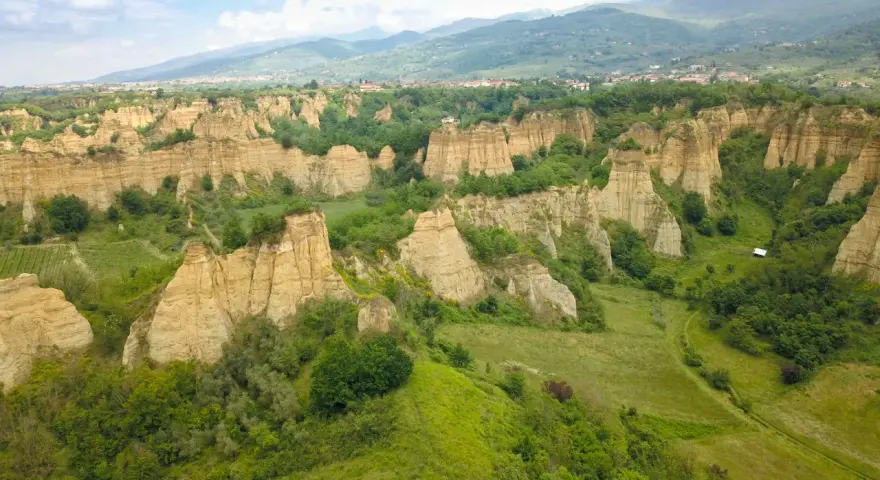 Le suggestive balze del Valdarno, scolpite dal tempo, si ergono tra verdi colline e un borgo in lontananza.