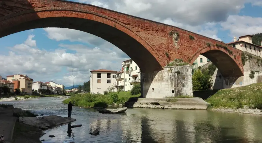 Ponte Mediceo a Pontassieve, cosa vedere: un pescatore sul fiume Sieve sotto l'arco in mattoni rossi, con case colorate sullo sfondo.