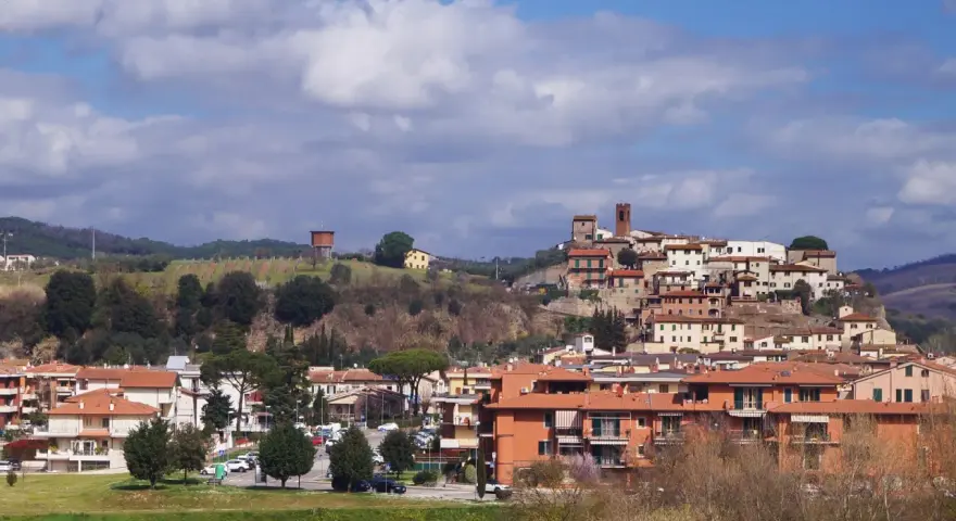 Paesaggio collinare con borgo medievale in cima, case moderne ai piedi. Si intravede un serbatoio d'acqua, vigneti e il **limite** del paese.