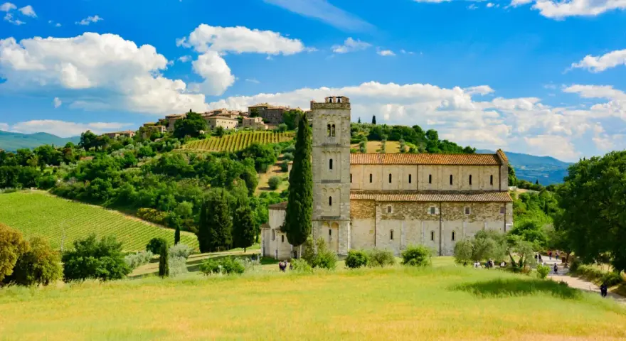 Abbazia di Sant'Antimo, un gioiello romanico immerso nel verde della Toscana, con vigneti e un borgo sullo sfondo.