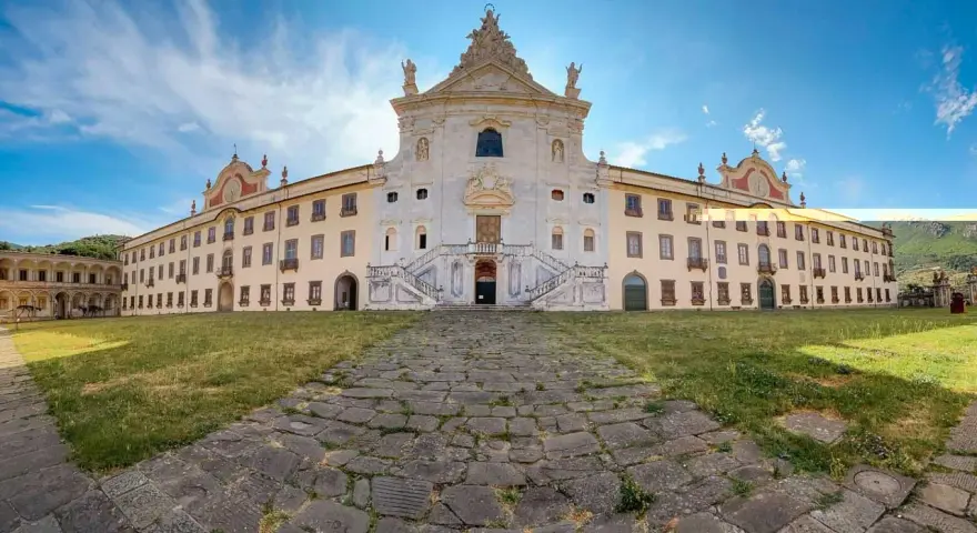 La maestosa Certosa di Calci si erge sotto un cielo azzurro, con un sentiero di pietra che conduce alla sua imponente facciata.