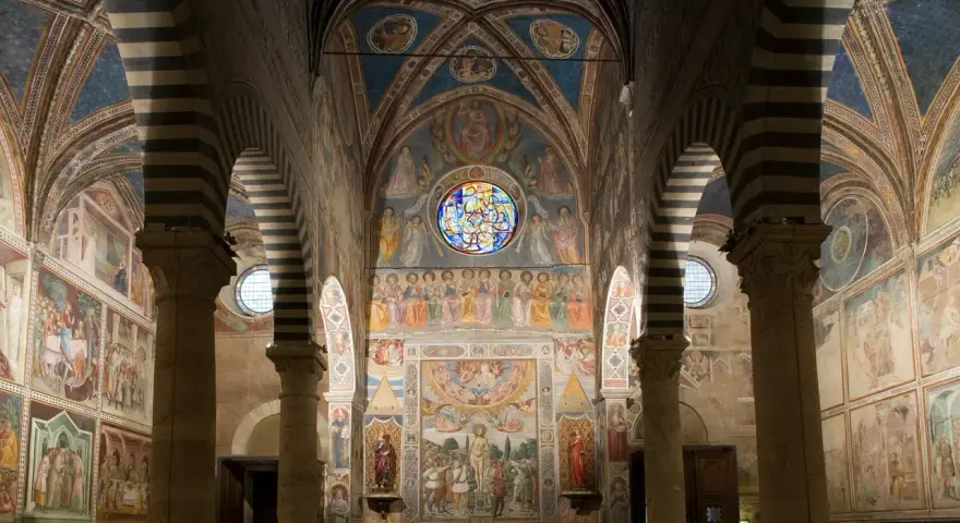 Interno del duomo di San Gimignano, con affreschi medievali che narrano storie sacre, volte a crociera a strisce bianche e nere e un rosone colorato.