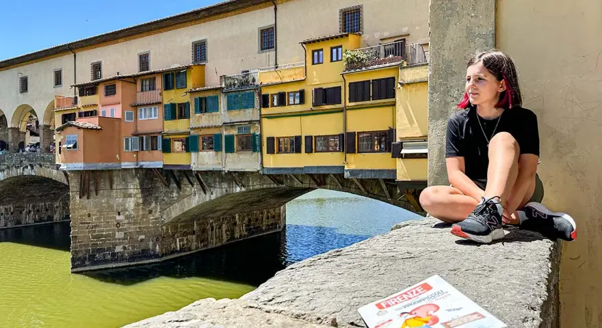 Ragazza con capelli rosa seduta sul Ponte Vecchio a Firenze, con una guida per bambini in primo piano.