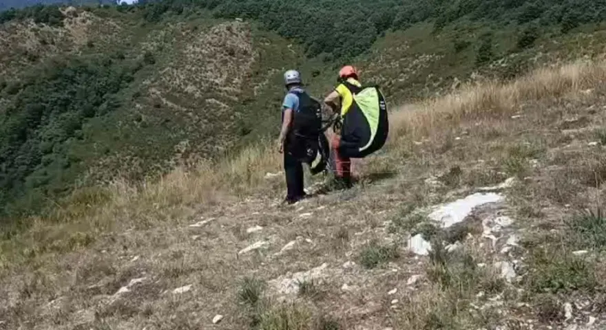 Due parapendisti si preparano al decollo sulla **Valle del Serchio**, con un paesaggio verdeggiante alle spalle.