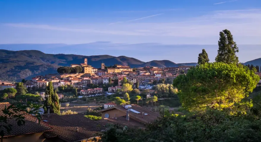 Panoramica di Montescudaio cosa vedere: borgo toscano con case in pietra, chiese e torri, immerso nel verde collinare sotto un cielo azzurro.