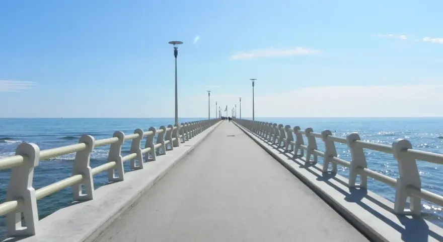 Il pontile di Forte dei Marmi si estende verso il mare azzurro sotto un cielo limpido, invitando a una passeggiata.
