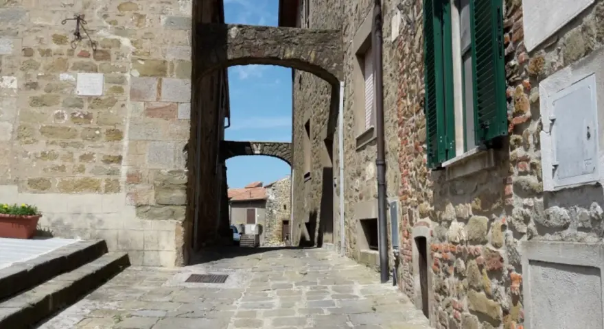 Un vicolo suggestivo a Vetulonia, tra antiche mura di pietra e archi che incorniciano il cielo azzurro. Scopri cosa vedere in questo borgo storico.