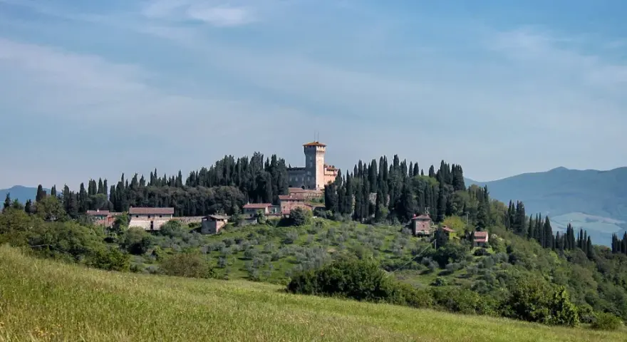 Un borgo collinare con un castello domina il paesaggio toscano di Scarperia e San Piero, circondato da cipressi e ulivi.