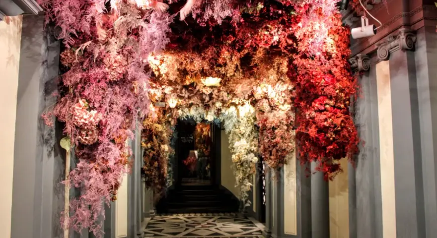 Ingresso fiorito, un arco di fiori rossi e rosa che ricorda l'antica farmacia di Firenze.