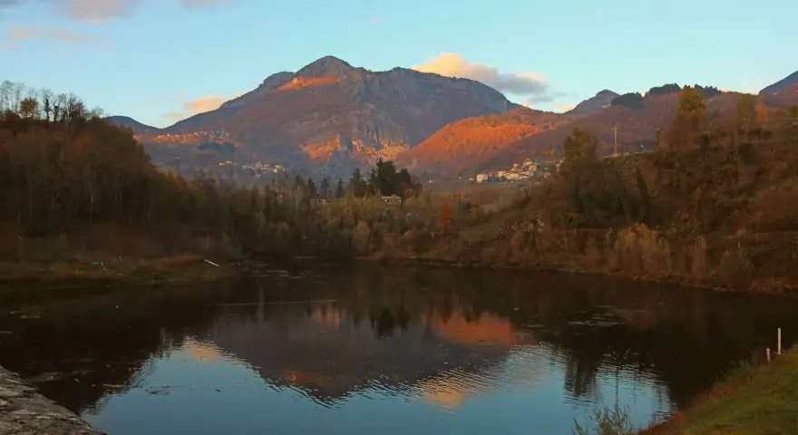 Tramonto dorato sulle montagne vicino a Villa Collemandina, con un lago che riflette il paesaggio autunnale.