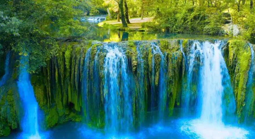 Cascata rigogliosa nel Val d'Arno, con acqua azzurra che scende su rocce ricoperte di muschio verde.