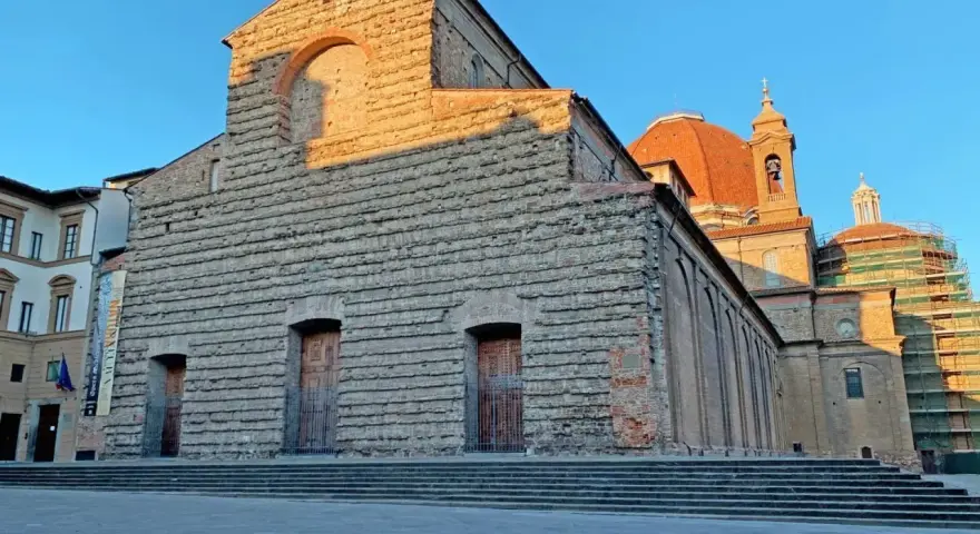 La facciata in pietra di San Lorenzo a Firenze, con la cupola arancione che domina il cielo azzurro.