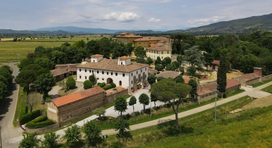 La Tenuta Frassineto, un complesso di edifici storici immerso nel verde, con campi coltivati e colline sullo sfondo.
