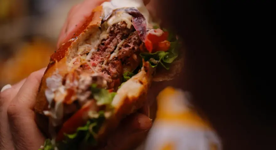 Mani che stringono un succulento hamburger, un'esplosione di sapori tipica dello street food ad Arezzo.