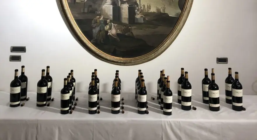 Bottiglie di vino Oreno della Tenuta Setteponti disposte su un tavolo, con un dipinto ovale sullo sfondo.