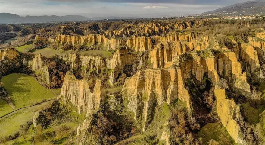 Paesaggio surreale nella provincia di Arezzo, con calanchi dorati che si ergono tra colline verdi e alberi spogli.