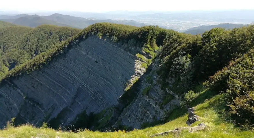 Panoramica mozzafiato sull'Alpe della Luna, con rocce stratificate che si ergono tra boschi rigogliosi e un cielo azzurro.