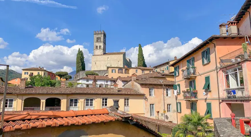 Panoramica di Barga, Lucca, con case colorate e il Duomo in cima alla collina sotto un cielo azzurro con nuvole bianche.