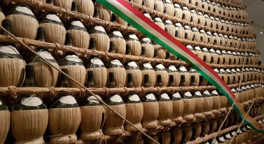 Una grande esposizione di bottiglie di vino impagliate, forse un omaggio alla tradizione della villa poggio reale rufina, con un tricolore italiano che le attraversa.