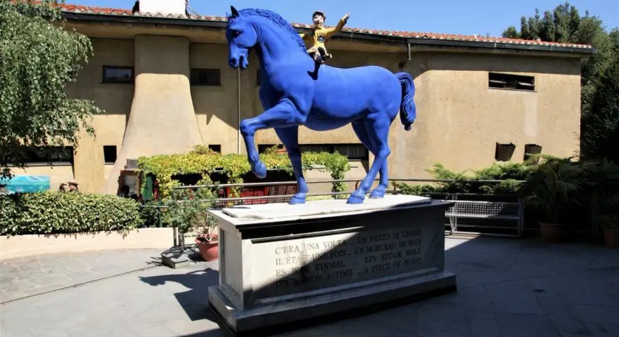 Un cavallo blu con Pinocchio a cavalcioni, simbolo del paese di Collodi. La statua è posta su un piedistallo con la frase "C'era una volta... un pezzo di legno" in più lingue.