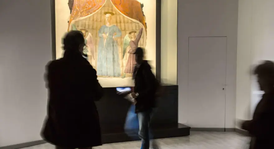 Un'opera d'arte a Monterchi, cosa vedere: visitatori ammirano un affresco con figure sacre in un museo.