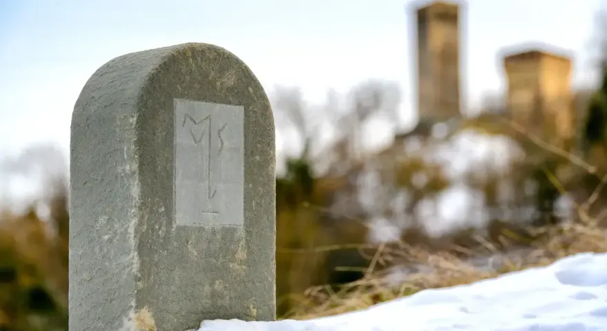 Monumento in pietra con simbolo inciso, sulla via Matildica del Volto Santo. In lontananza, castelli innevati.