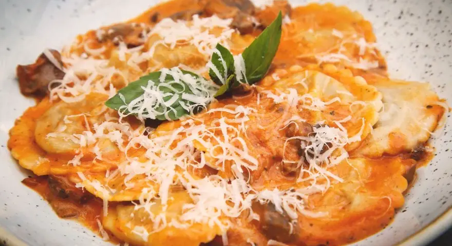Tordelli versiliesi in un piatto bianco, conditi con sugo rosso, funghi, parmigiano grattugiato e basilico fresco.