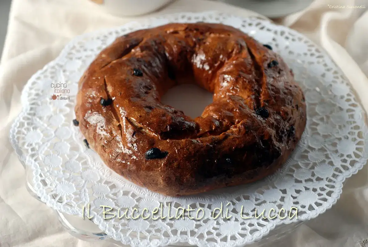 Il Buccellato di Lucca, un dolce tradizionale lucchese, è un pane dolce a forma di ciambella con uvetta, servito su un centrino di pizzo.