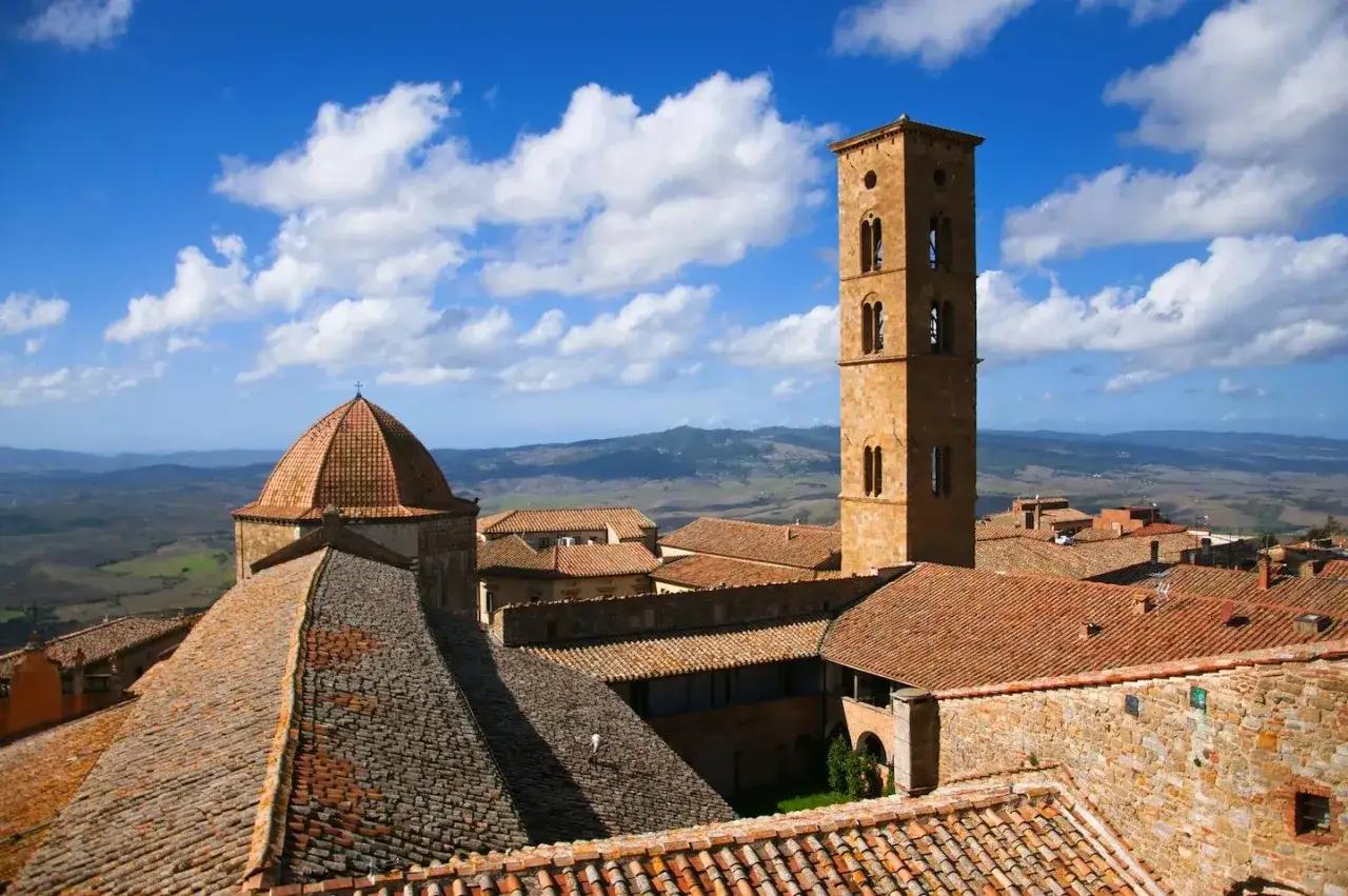 Torre campanaria e cupola di chiese a Volterra, tra i tetti rossi e il paesaggio toscano. Cosa vedere in questa città storica.