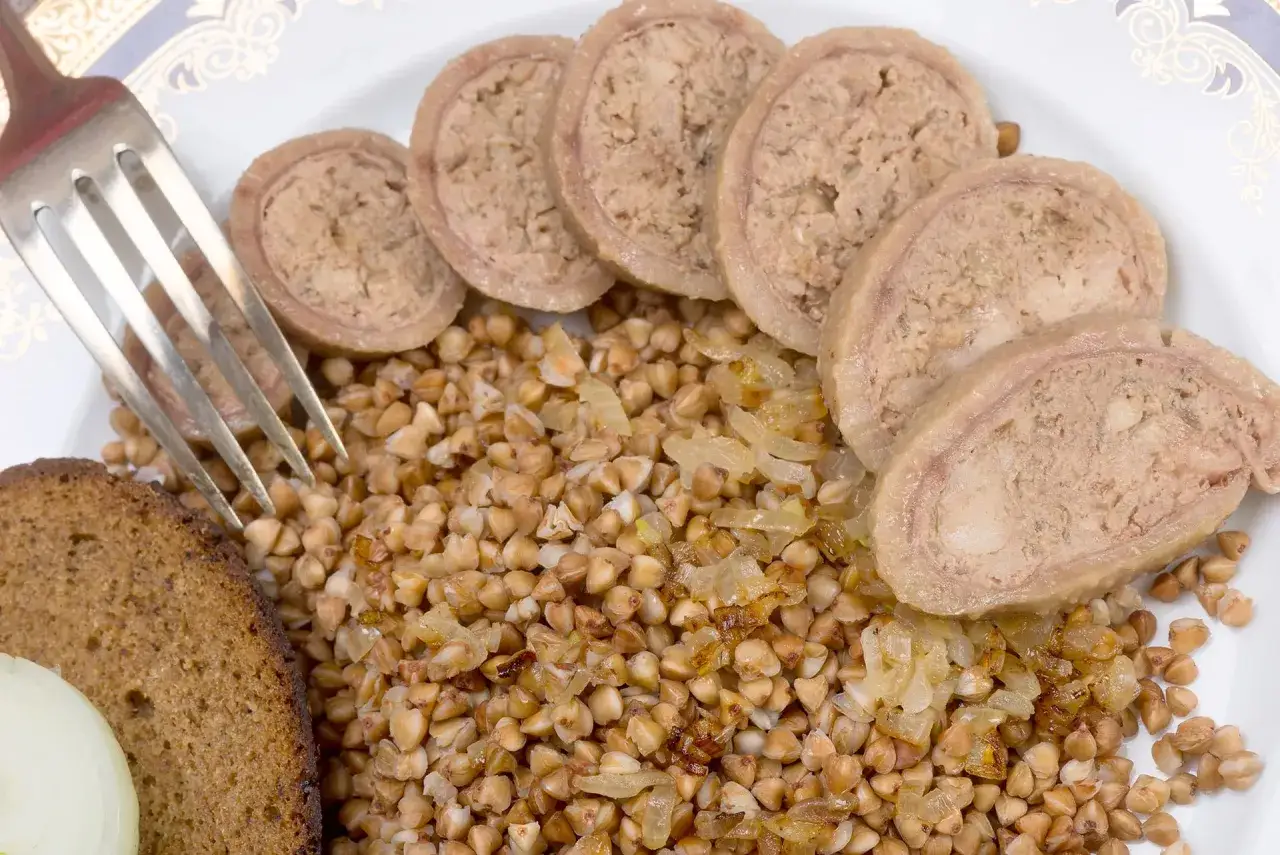 Fetta di pane scuro, grano saraceno con cipolle e fette di collo ripieno su un piatto bianco.