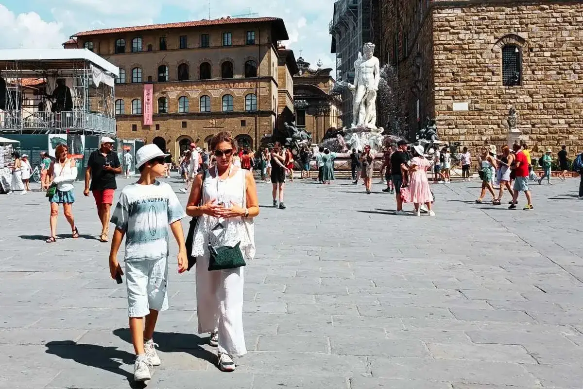 Una donna e un ragazzo passeggiano in una piazza di Firenze, tra turisti e la fontana del Nettuno. Un'indimenticabile gita a Firenze con bambini.