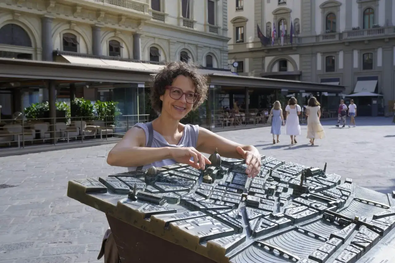 Donna sorride mentre studia una mappa in bronzo del centro storico di Firenze, con edifici storici e il Duomo in miniatura.