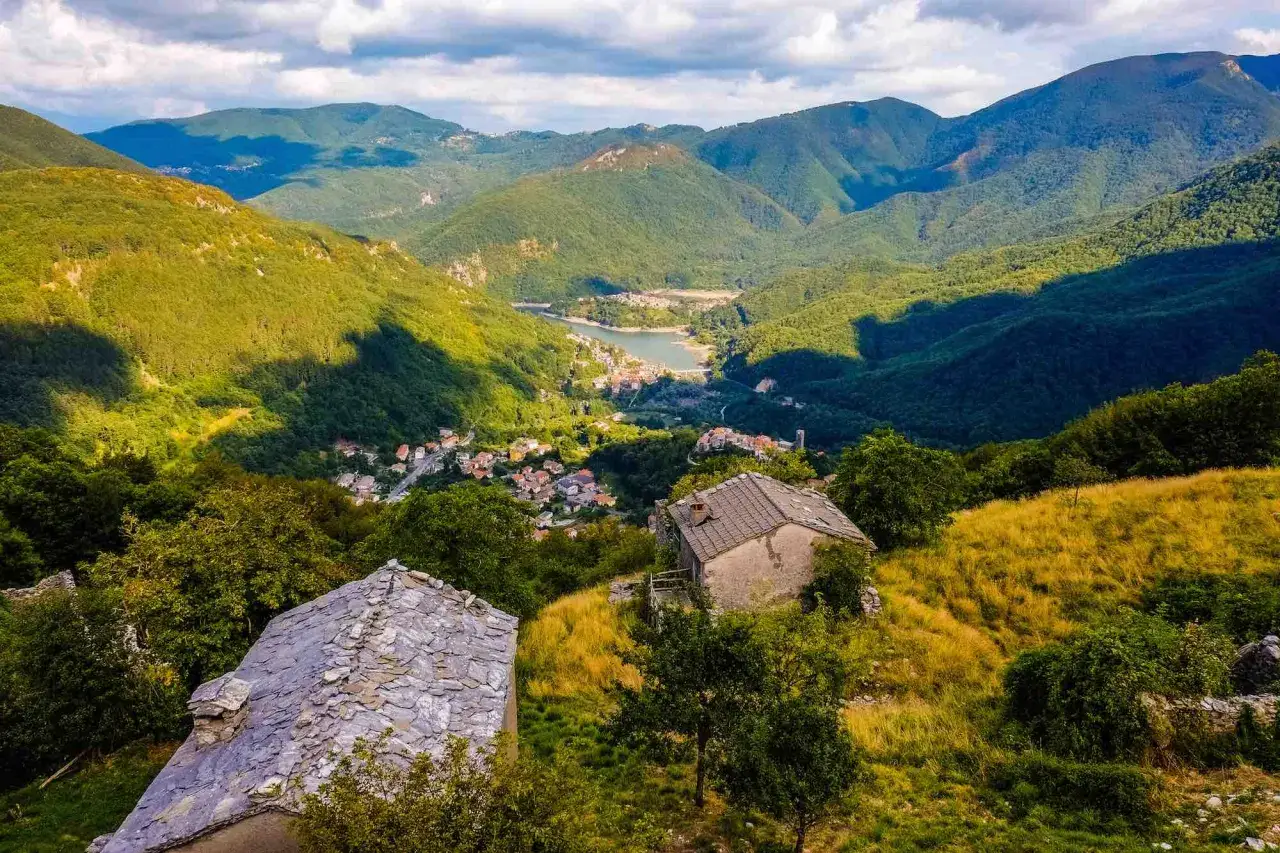 Panoramica sulla valle del Serchio con case in pietra e un lago incastonato tra le montagne verdi.