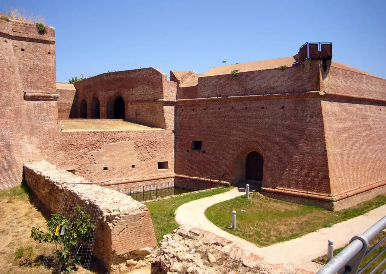 Fortificazioni in mattoni rossi a Grosseto, Italia, con un sentiero curvo che conduce a un portale ad arco.