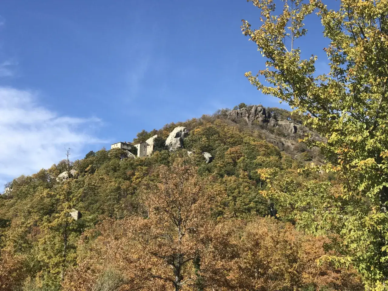 L'eremo di Cerbaiolo, incastonato tra alberi autunnali e rocce, si staglia contro un cielo azzurro.