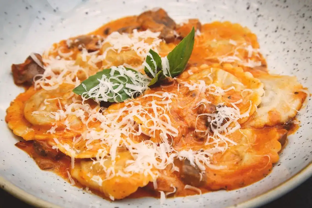 Tordelli versiliesi in un piatto bianco, conditi con sugo rosso, funghi, parmigiano grattugiato e basilico fresco.