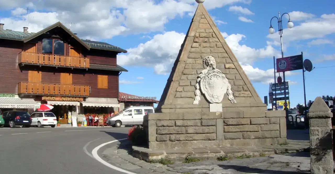 Le piramidi dell'Abetone, un monumento in pietra con uno stemma, si ergono accanto a un edificio in legno con balconi e negozi.