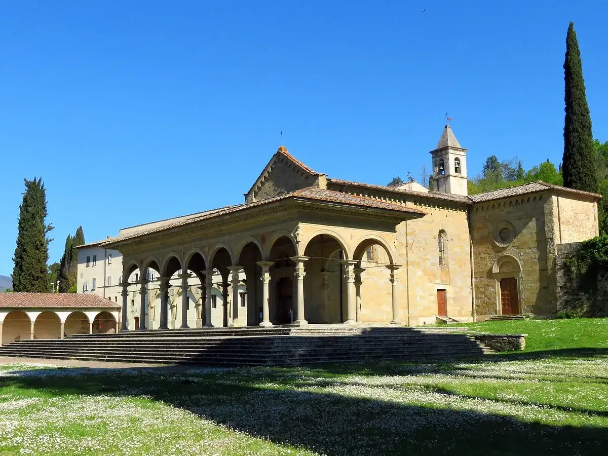 Arezzo, Santa Maria delle Grazie: portico ad archi, campanile e prato fiorito sotto un cielo azzurro.